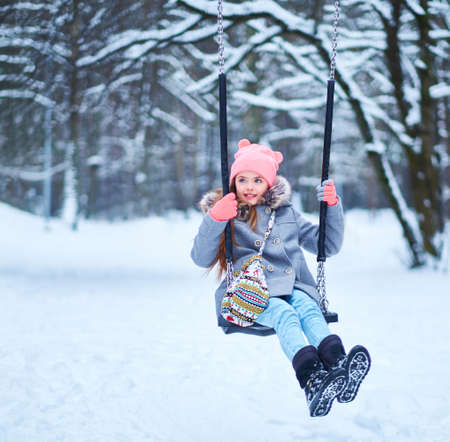 Charming little girl on swing in snowy winterの写真素材