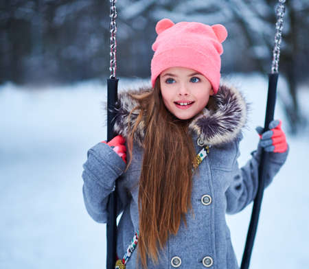 Charming little girl on swing in snowy winterの写真素材