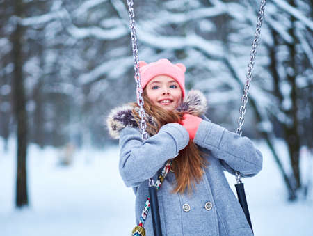 Charming little girl on swing in snowy winterの写真素材