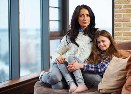 Beautiful little girl and her mother sitting on a couchの写真素材