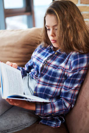 Pretty little girl reading book on a couchの写真素材
