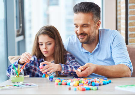 Beautiful little girl with her father playing with colored set for creativityの写真素材