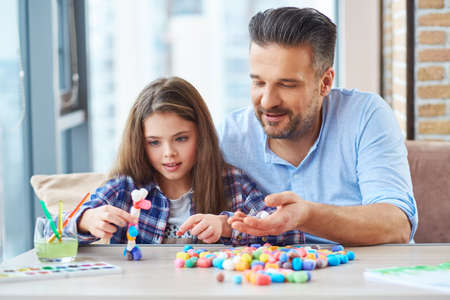 Beautiful little girl with her father playing with colored set for creativityの写真素材