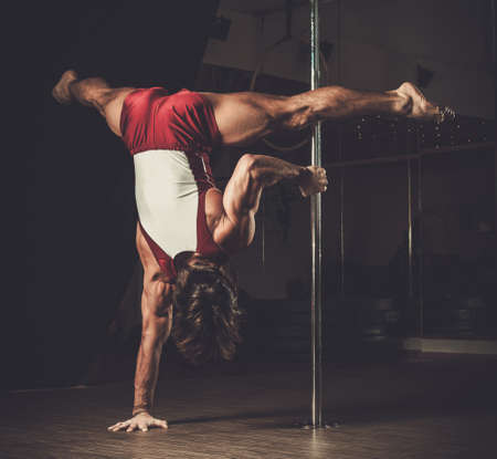 Handsome man performing pole dance moves on pole