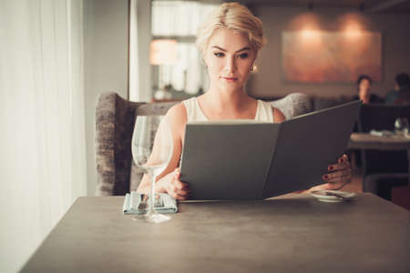 Elegant blonde woman with menu in a restaurantの写真素材