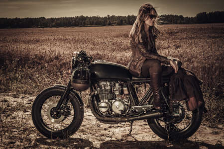 Young, stylish woman on vintage custom cafe racer in fieldの写真素材
