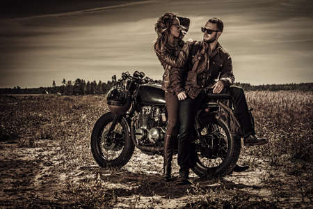 Young, stylish cafe racer couple on vintage custom motorcycles in fieldの写真素材