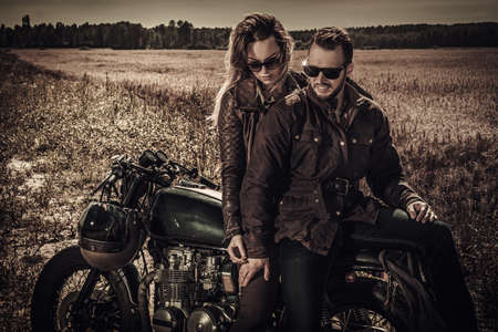 Young, stylish cafe racer couple on vintage custom motorcycles in field.の写真素材