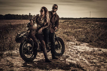 Young, stylish cafe racer couple on vintage custom motorcycles in fieldの写真素材