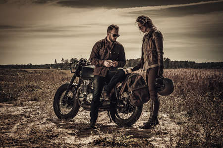 Young, stylish cafe racer couple on vintage custom motorcycles in fieldの写真素材