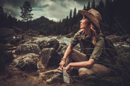 Woman hiker searching right direction on map near wild mountain riverの写真素材