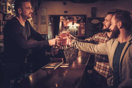 Cheerful old friends drinking draft beer at bar counter in pub.の写真素材