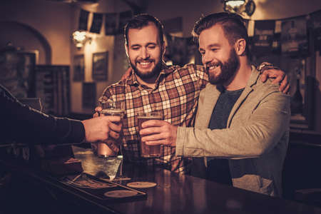 Cheerful old friends drinking draft beer at bar counter in pub.の写真素材