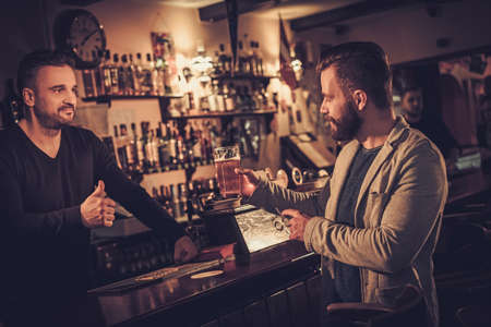 Stylish man paying for beer by card to bartender in pub.の写真素材