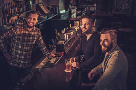 Cheerful old friends drinking draft beer at bar counter in pub.の写真素材