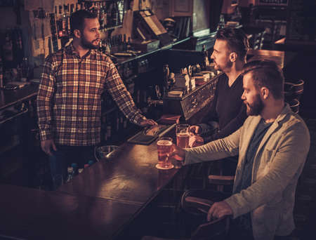 Cheerful old friends drinking draft beer at bar counter in pub.の写真素材