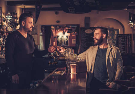 Stylish man paying for beer by card to bartender in pub.の写真素材