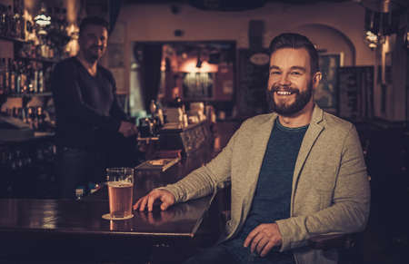 Stylish man sitting alone at bar counter with a pint of light beer.の写真素材