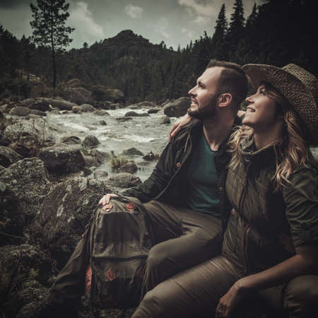 Cheerful couple hikers sitting near wild mountain river.の写真素材