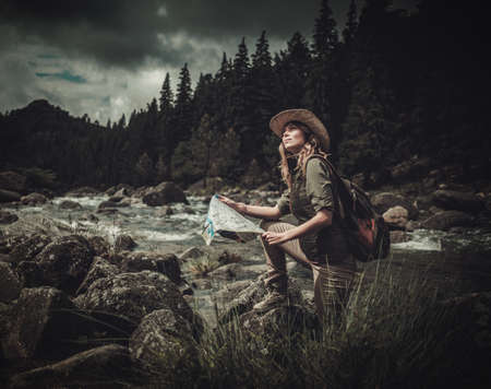 Woman hiker, searching right direction on map near wild mountain river.の写真素材