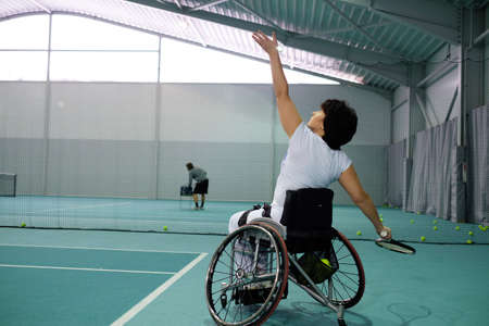 Disabled mature woman on wheelchair playing tennis on tennis court.の写真素材