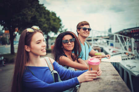 Multi-ethnic friends tourists with map and coffee cups near river in a cityの写真素材