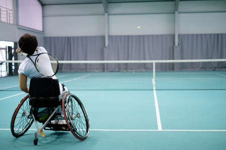 Disabled mature woman on wheelchair playing tennis on tennis court.の写真素材