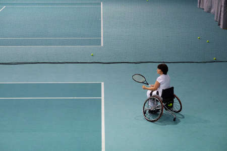 Disabled mature woman on wheelchair playing tennis on tennis court.の写真素材