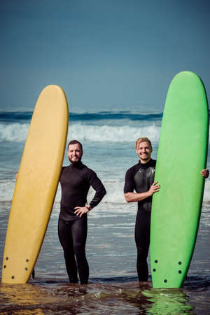 Surfer beginner and instructor on a beach with a surfboardsの写真素材
