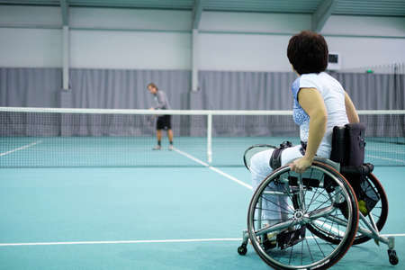 Disabled mature woman on wheelchair playing tennis on tennis court.の写真素材