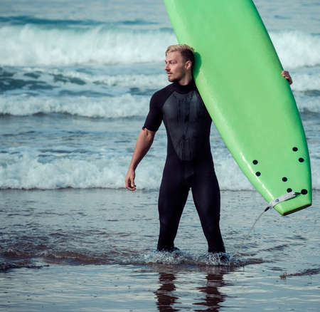 Surfer wearing wetsuit standing on the beach with a surfboardの写真素材