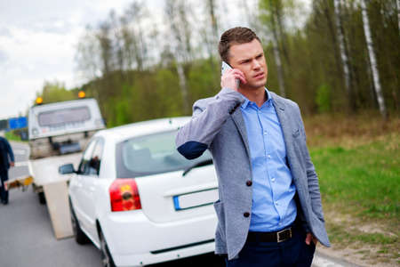 Man calling while tow truck picking up his broken carの写真素材