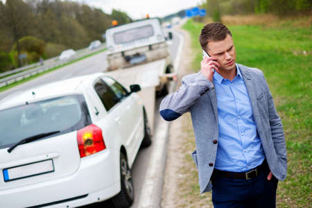 Man calling while tow truck picking up his broken carの写真素材