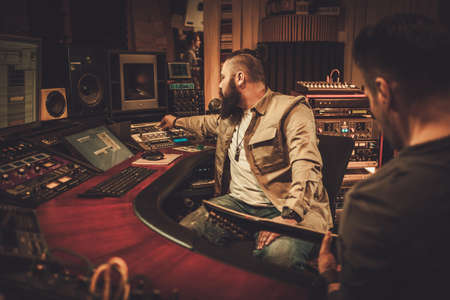 Sound engineer and guitarist recording song in boutique recording studio.