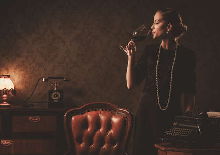 Beautiful woman with glass of wine in retro interiorの写真素材