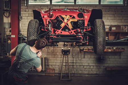Mechanic working on classic car wheels and suspension in restoration workshop.