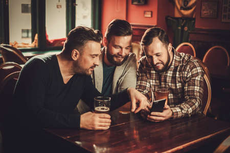 Cheerful old friends having fun and drinking draft beer in pub.
