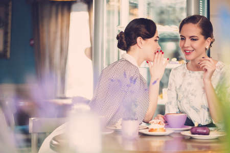 Two elegant young ladies talking secrets in a cafeの写真素材