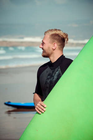 Surfer wearing wetsuit standing on the beach with a surfing boardの写真素材