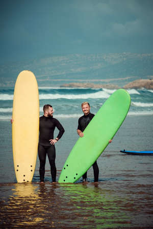 Surfer beginner and instructor on a beach with a surfing boardsの写真素材