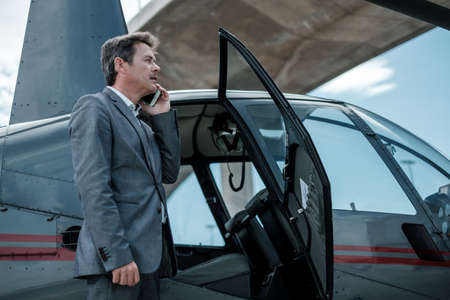 Businessman talking on cellphone near private helicopter