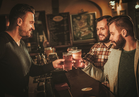 Old friends having fun and drinking draft beer at bar counter in pub.の写真素材