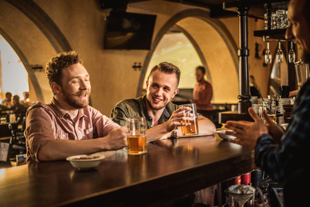 Cheerful friends drinking draft beer in a pubの写真素材