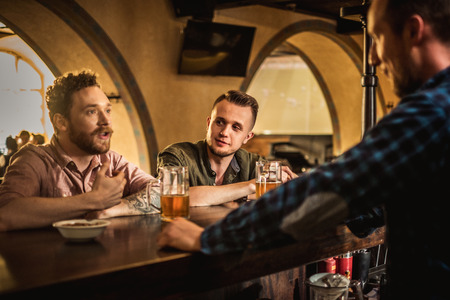 Cheerful friends drinking draft beer in a pubの写真素材