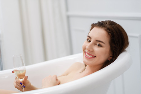 Woman laying in a bath with glass of champagneの写真素材
