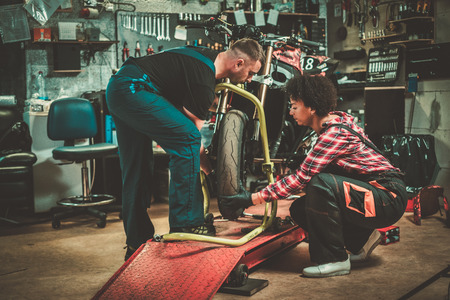 Mechanic and his helper repairing a motorcycle in a workshopの写真素材