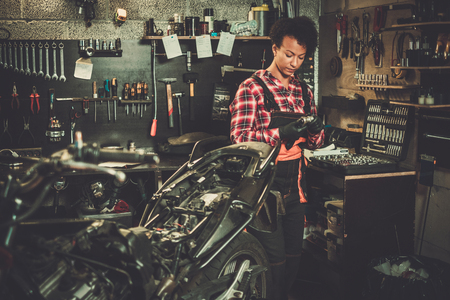 African american woman mechanic repairing a motorcycle in a workshopの写真素材