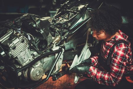 African american woman mechanic repairing a motorcycle in a workshopの写真素材