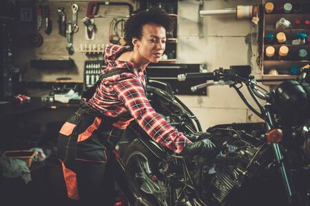 African american woman mechanic repairing a motorcycle in a workshopの写真素材