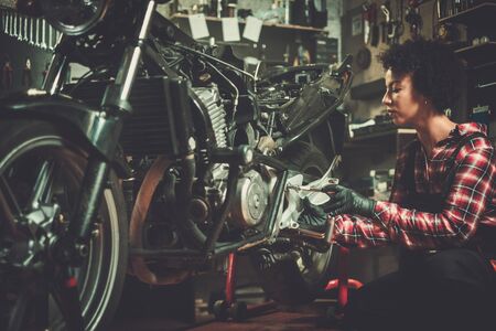 African american woman mechanic repairing a motorcycle in a workshopの写真素材